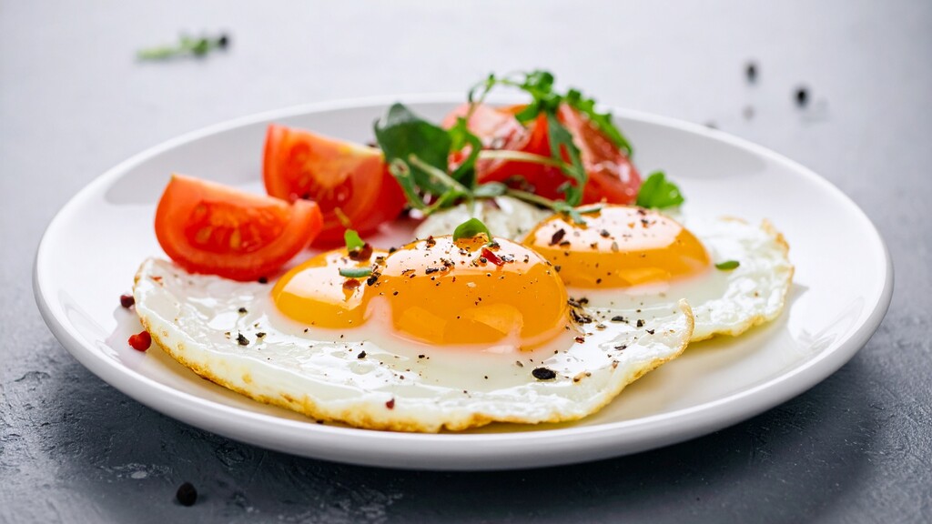 Two sunny-side-up eggs served with tomatoes and herbs on a white plate.