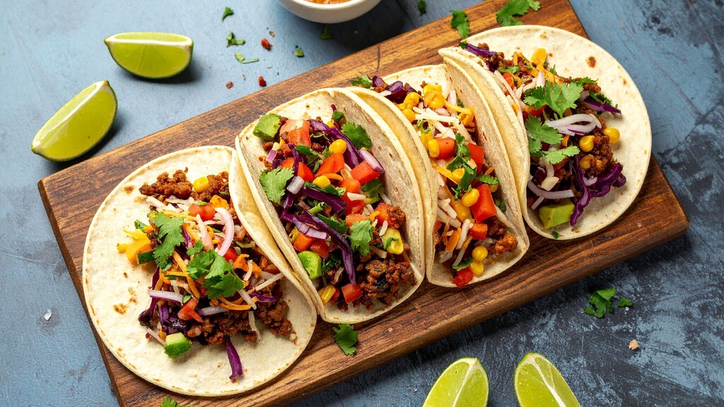 Ground turkey tacos with colorful cabbage slaw, corn, avocado, cilantro, and lime wedges.