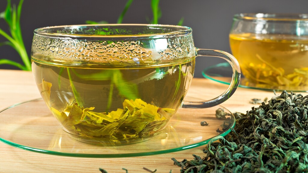 Cup of green tea with loose tea leaves on a wooden table.