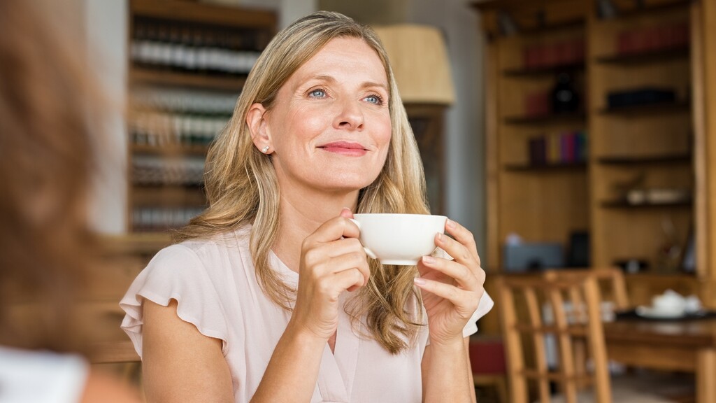 Thoughtful woman holding a cup of tea in a warm home setting, reflecting on early changes in her health.