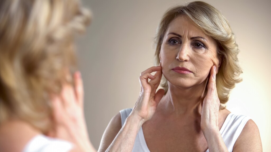 Woman examining her jawline and neck in a mirror, noticing possible skin changes linked to metabolic health.