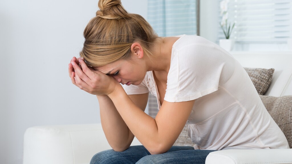 A tired woman sitting on a couch with her head in her hands, representing stress and fatigue during a weight loss plateau.