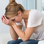 The Biological Reasons You Are Not Losing Weight in a Calorie Deficit A tired woman sitting on a couch with her head in her hands, representing stress and fatigue during a weight loss plateau.