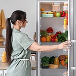 Woman opening an organized refrigerator filled with fresh fruits, vegetables, and prepared foods for healthier daily choices.