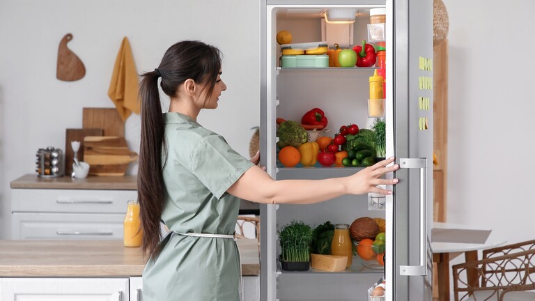Woman opening an organized refrigerator filled with fresh fruits, vegetables, and prepared foods for healthier daily choices.