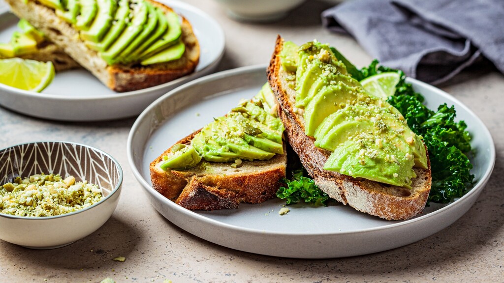 Avocado toast on sourdough bread served with greens and lime.