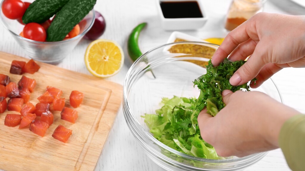 Hands preparing a fresh salmon salad with lettuce, vegetables, lemon, and dressing for a healthy weight loss meal.