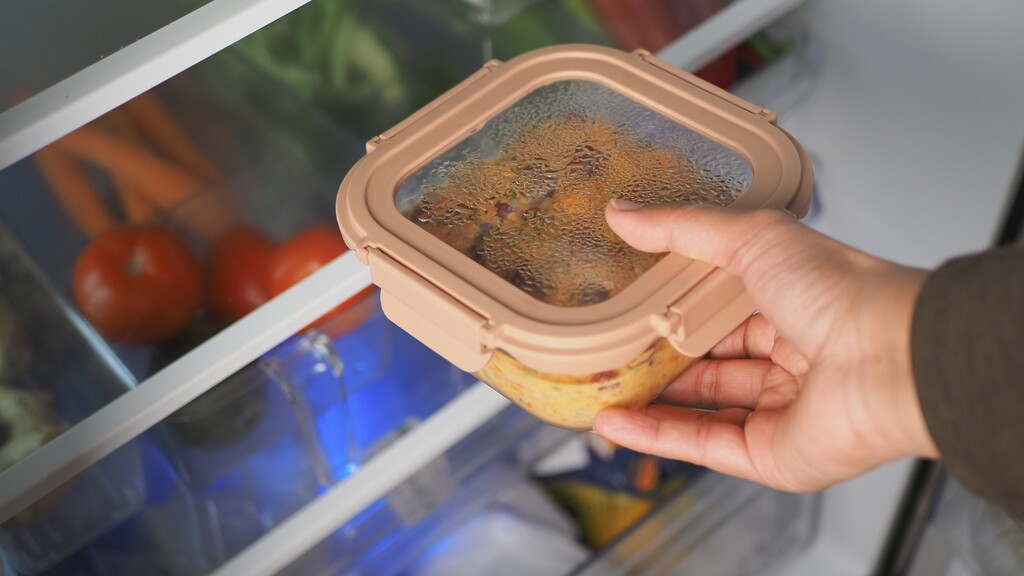 Hand placing a clear meal prep container in the refrigerator to keep prepared healthy food visible and easy to grab.