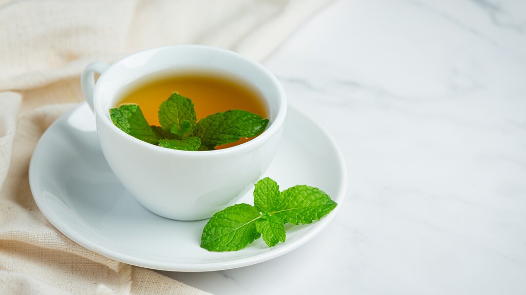 Cup of peppermint tea with fresh mint leaves on a white saucer.