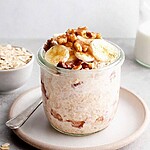 A glass jar of thick chia overnight oats topped with banana slices, walnuts, and a dusting of cinnamon