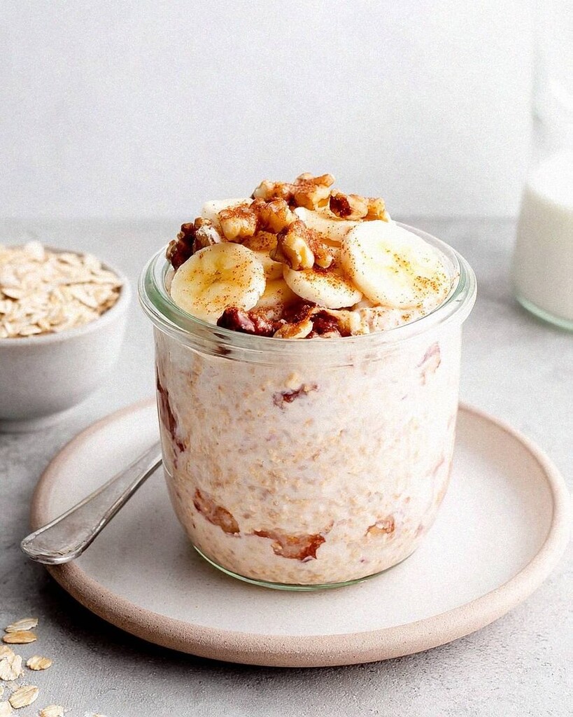 A glass jar of thick chia overnight oats topped with banana slices, walnuts, and a dusting of cinnamon